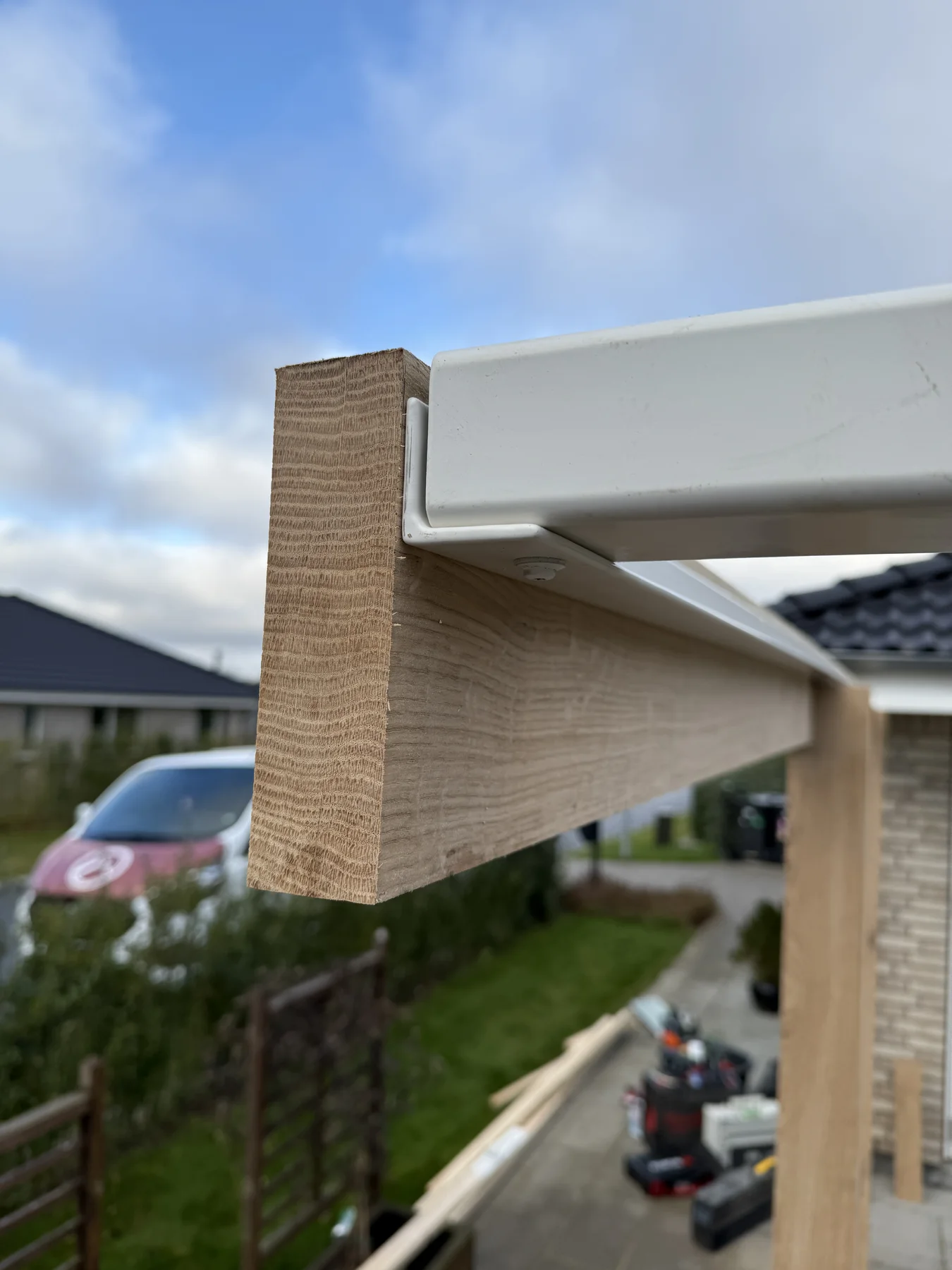 Et nærbillede af en træbjælke, der er monteret i en bærende konstruktion af hvidmetal udendørs, med byggematerialer og værktøj synlige i baggrunden – hvilket viser det dygtige tømrerhåndværk og den sans for detaljer, som Tømrerfirmaet Kenn leverer.